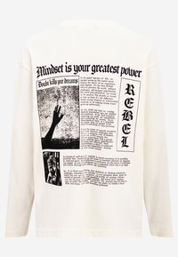 White long-sleeve t-shirt featuring black printed text and images on the back. Distinctive graphics include hands and various typographic elements.