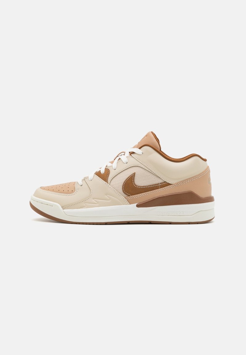 Baskets Nike beige et marron à tige basse avec lacets blancs, bout perforé et semelle en caoutchouc, vues de profil sur fond blanc.
