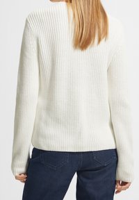 Biały sweter z dzianiny o teksturowanym wzorze, z długimi rękawami i luźnym krojem, zestawiony z ciemnoniebieskimi dżinsami.