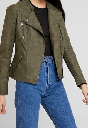 Olijfgroene neplederen motorjack met schouderepauletten, asymmetrische rits en twee ritszakken aan de voorkant, gecombineerd met high-waisted jeans.