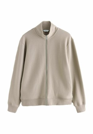 Beige ribbed zip-up jacket with long sleeves and a high collar, featuring a visible silver zipper down the front.