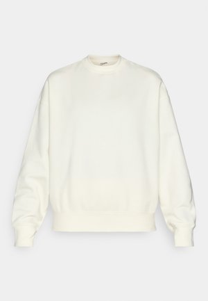 Kreemivärvi dressipluus, mis on valmistatud pehmest kangast. Omab ümarat kaelust, kukkunud õlgu ning soonikuid mansetidel ja äärel. Lihtne disain ilma mustriteta.