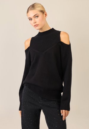 Schwarzer Strickpullover mit hohem Kragen, offenen Schultern und gerippter Textur. Das Design weist ein V-förmiges Detail am Ausschnitt auf.