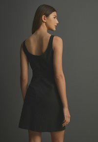 Robe noire sans manches avec un dos décolleté, un corsage ajusté et une jupe évasée. Tissu lisse avec un subtil détail de couture.
