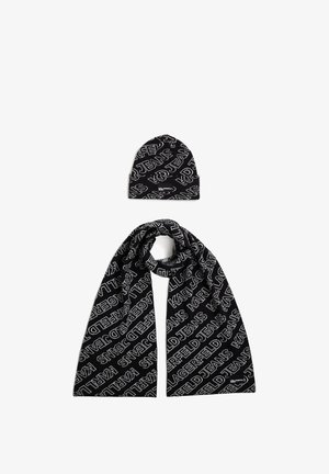 Conjunto de cachecol e gorro de malha preta com padrão de texto branco repetido. Textura suave, forma estruturada, com logótipos em destaque.