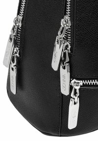Czarna skórzana torba o teksturze z wieloma srebrnymi zamkami błyskawicznymi, z metkami marki na uchwytach zamków i wyprofilowanym dolnym kształtem.