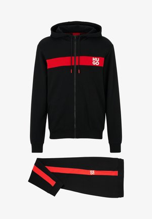 Čierna mikina s kapucňou a zodpovedajúce nohavice. Obsahuje červený horizontálny pruh s logom, zips na zapínanie, kontrastné šnúrky a jemnú textúru látky.