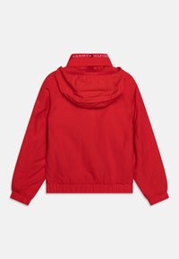 Rød hættetrøjejakke lavet af letvægtsmateriale med elastiske manchetter og taljebånd samt "TOMMY HILFIGER"-logo på kraven.