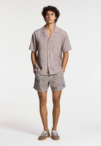 Set kratkih rukava i kratkih hlača od tkanine s uzorkom u smeđim, plavim i krem bojama s geometrijskim dizajnom. Ležeran kroj.