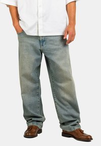 Helle blaue Denim-Jeans mit lockerem Schnitt, ausgestattet mit einem klassischen Fünf-Taschen-Design und subtiler, verblasster Textur, kombiniert mit braunen Schuhen.