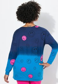 Camicia a maniche lunghe blu con sfumatura dal navy al turchese, caratterizzata da un motivo di faccine sorridenti nere e rosa sparse. Tessuto morbido.