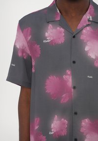 Short-sleeve, button-up shirt in gray fabric featuring large pink floral patterns and subtle branding in white on the collar and sleeve.