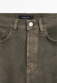 Pantalon en denim vert olive avec une braguette standard à glissière, une poche avant et une fermeture à bouton argenté. L'étiquette indique "Massimo Dutti".