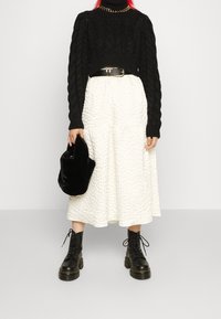 Czarny sweter o splocie warkoczowym, biała teksturowana spódnica midi, czarny pasek w talii, puszysta czarna torebka oraz czarne platformy na sznurowania.