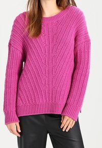 Rosa stickad tröja med texturerade kabelmönster, rund halsringning och långa ärmar. Ribbstickad nederkant, avslappnad passform och mjuk textur.