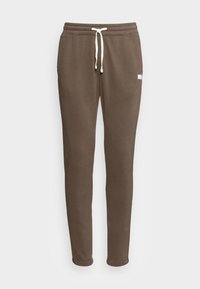 Hnědé tepláky vyrobené z měkké látky, s elastickým pasem a bílými šňůrkami na stažení, s tapered nohavicemi. Jednoduchý design bez vzorů.