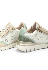Zapatillas en beige y verde menta con cuero blanco perforado, cremalleras doradas y una suela blanca gruesa. Acentos texturizados en los laterales.