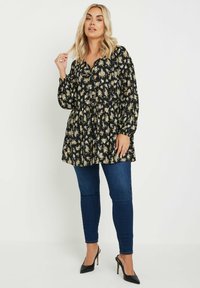 Svart blommig tunika med långa ballongärmar, har en r gathered midja och knappar. Matchad med mörkblå slim-fit jeans och svarta klackar.