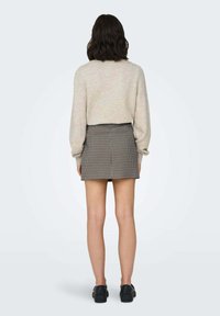 Pull gris avec des manches longues légèrement bouffantes, associé à une mini-jupe ajustée à carreaux noir et blanc. Des chaussures noires complètent le look.