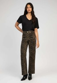 T-shirt noir à col en V associé à un pantalon en imprimé léopard marron taille haute. Le modèle porte des bottines noires. Style simple et décontracté.