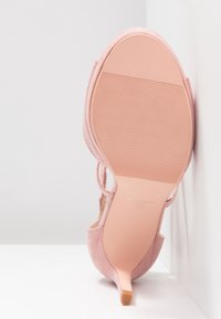 Chaussure à talon haut en daim rose unique reposant sur une surface blanche, semelle tournée vers l'avant, montrant la pointure 37 et le nom de la marque en dessous.