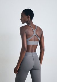Grå sportbh med korsryggdesign och matchande hightwaisted leggings. Slät textur med minimala sömmar och en åtsittande silhuett.
