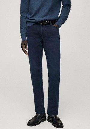 Dark blue jeans with a straight fit, made from denim. The outfit is paired with black loafers and a black belt.