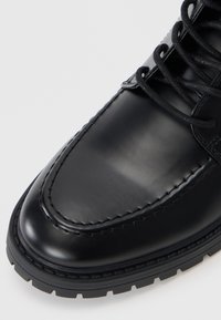 Zapato de cuero negro con un diseño elegante, punta redonda, detalles cosidos y suela de goma negra texturizada con patrones de agarre.