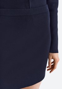 Abito aderente in maglia blu navy con una texture liscia, maniche lunghe e un delicato dettaglio in vita. Progettato per una silhouette su misura.