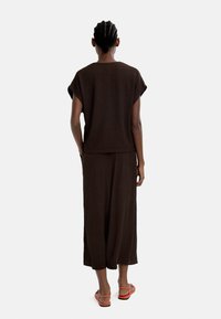 Brązowy, teksturowany zestaw składający się z dwuczęściowego stroju, z bluzką z krótkim rękawem i spodniami z szerokimi nogawkami, zestawiony z czerwonymi płaskimi sandałami. Prosty design, luźny krój.