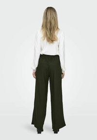 Grønne bredbenede bukser med en tekstureret finish, der har en elastisk talje. Sammen med en hvid langærmet top med sammenfoldede skuldre.