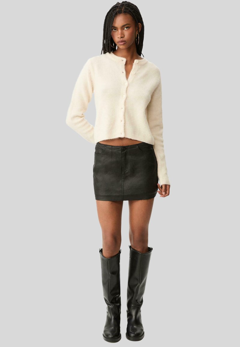 Beige, cropped cardigan met knoopsluiting, gecombineerd met een zwarte denim minirok en hoge zwarte leren laarzen. Glad textuur, getailleerd ontwerp.