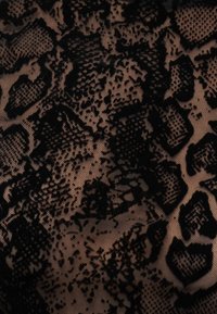 Μαύρο δαντελένιο ύφασμα με floral και γεωμετρικό μοτίβο πάνω σε μπεζ φόντο, που δείχνει λεπτομερή υφή και περίπλοκο σχέδιο.