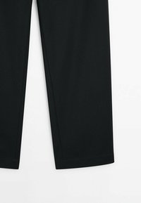 Pantalon noir à jambes droites montré de la hauteur du genou vers le bas sur fond blanc, avec des ourlets nets et une texture de tissu lisse.