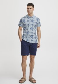 Ljusblå pikétröja med ett blommönster i mörkblått, ihopparad med marinblå shorts. Outfiten kompletteras med bruna sandaler.