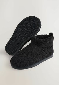 Papuci de antracit, cu textură din fleece, pentru gleznă, având talpă din cauciuc; unul este prezentat cu talpa în sus, având mărimea 42 și numele brandului "NEXT" vizibil.