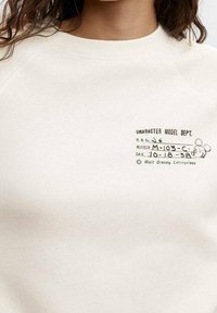 Kreativ farvet sweatshirt i creme med rund hals, der har et trykt grafik af "Character Model Dept." og et Mickey Mouse ikon.