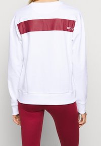 Vit sweatshirt med ett brett vinröd rand över ryggen och texten "EST. 93". Mjukt tyg och ribbade ärmslut med avslappnad passform.