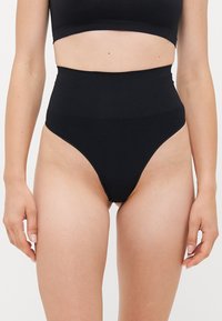 Woman wearing high-waisted black shapewear underwear and matching black crop top, shown from mid-torso to upper thighs.