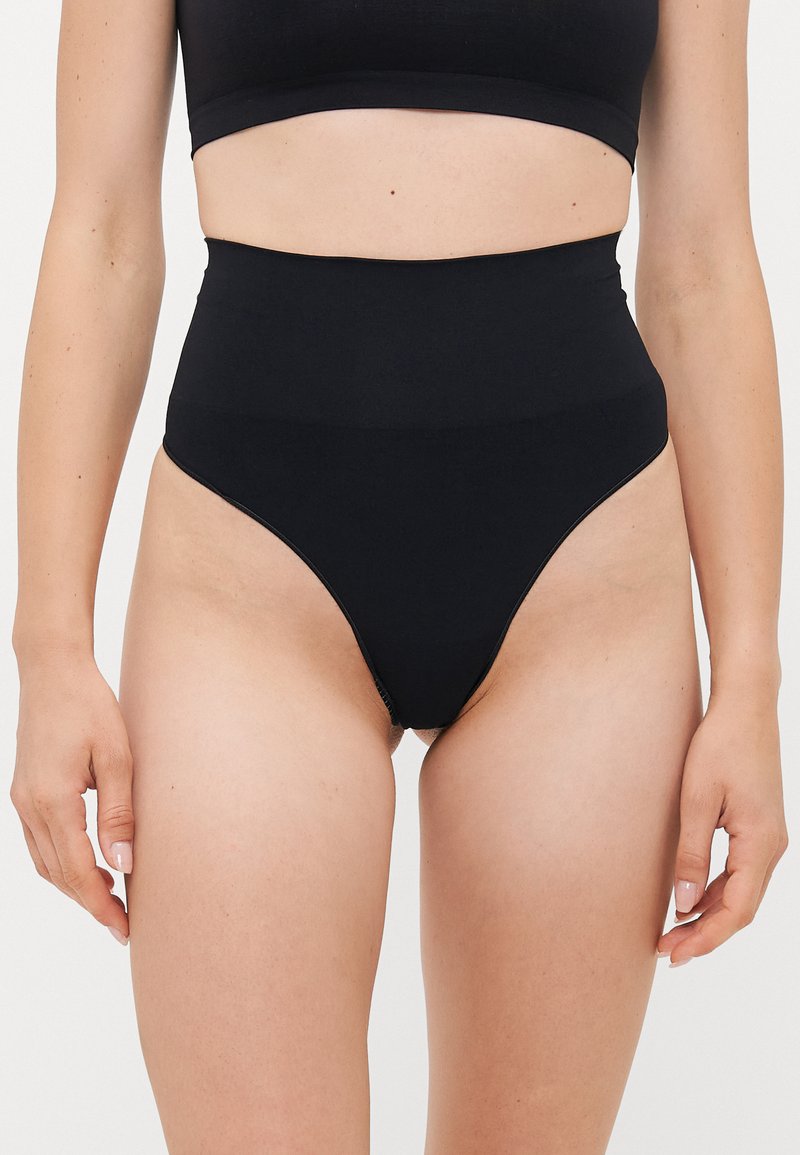 Woman wearing high-waisted black shapewear underwear and matching black crop top, shown from mid-torso to upper thighs.