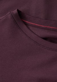 Bordeaux t-shirt met een ronde hals en een contrasterende rode stiksel, gemaakt van zachte, gladde stof met een aansluitende pasvorm.
