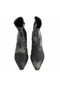 Botines de denim negro hasta el tobillo con puntera afilada, acabado texturizado, cremalleras laterales y suelas de goma planas. Presenta manchas sutiles en tonos grises.