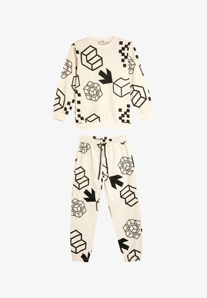 Crème-kleurige sportoutfit met geometrische zwarte patronen, waaronder kubussen en pijlen. De top heeft lange mouwen; de broek heeft een elastische tailleband.