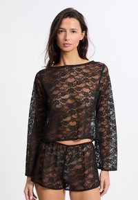 Top de encaje negro con mangas largas y cuello redondo, combinado con pantalones cortos de encaje a juego. Textura transparente con detalle de patrón floral.