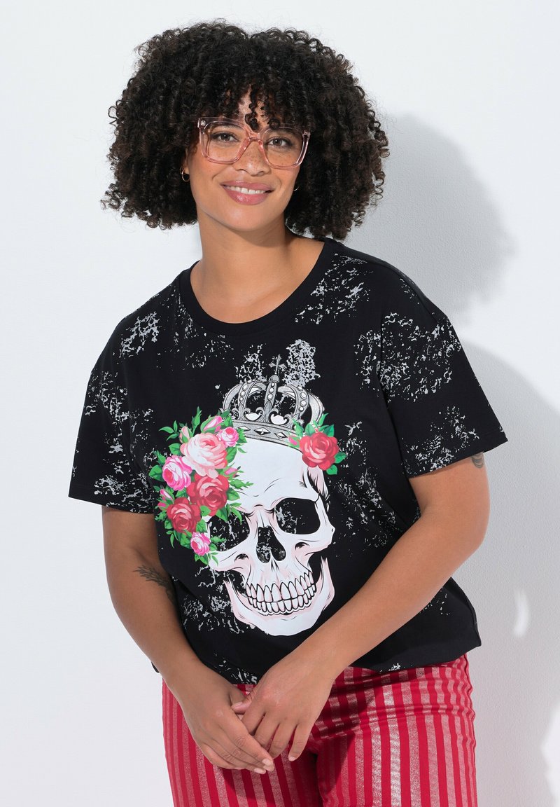 Camiseta gráfica negra con un gran cráneo rodeado de rosas rosas y una corona, con una textura desgastada. Combinada con pantalones de rayas rojas.