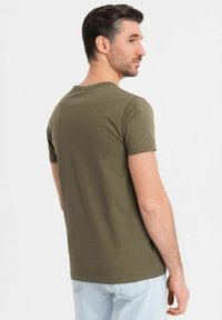Camiseta de manga corta color verde oliva, hecha de algodón, con un clásico escote redondo y un corte ajustado, y con una etiqueta en el lateral.