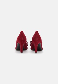 Escarpins en daim rouges avec des pointes effilées et un nœud décoratif à l'arrière. Semelles en caoutchouc noir avec une hauteur de talon modérée.