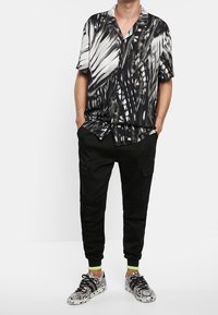 Uomo che indossa una camicia a maniche corte con stampa astratta in bianco e nero, pantaloni jogger cargo neri e sneakers a motif bianco e nero.