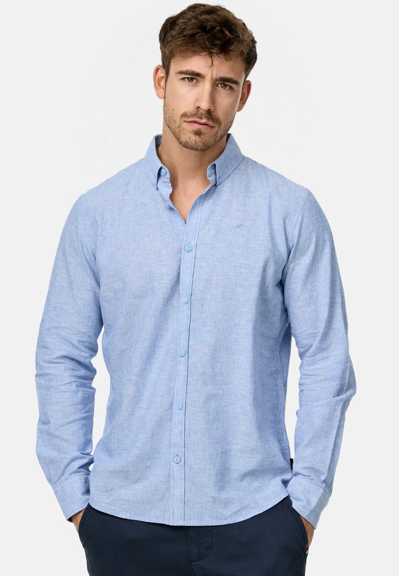 Chemise boutonnée à manches longues de couleur bleu clair avec un tissu texturé, présentant un col pointu et une fermeture à boutons sur le devant. Motif rayé subtil.