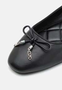 Bailarinas de cuero negro con punta redonda, nudo decorativo con acentos plateados y superficie texturizada sutil.